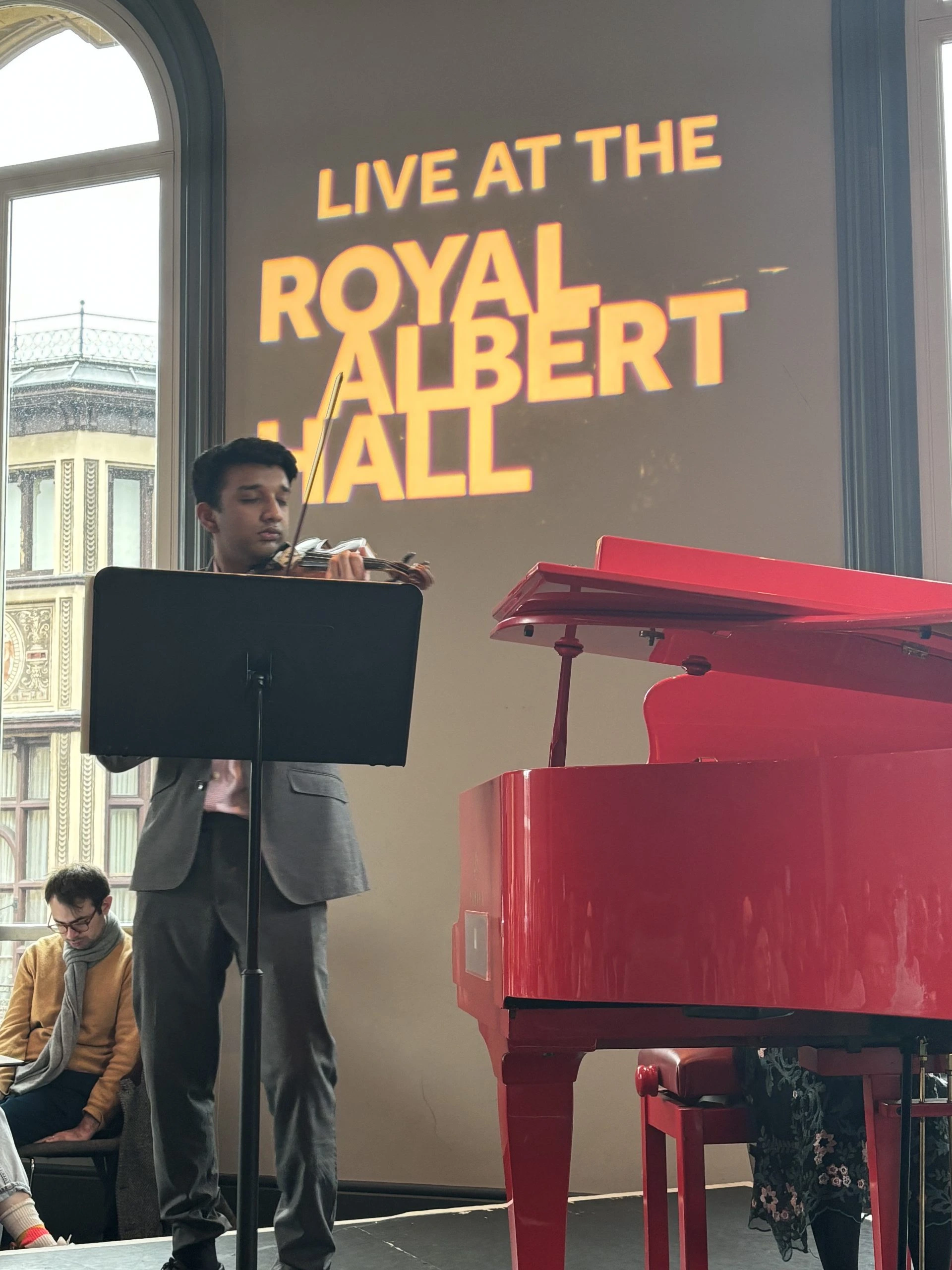 Vivek Dinesh Ramanan playing the violin in the Royal Albert Hall next to a red piano